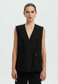 Schwarze ärmellose Wickelweste mit tiefem V-Ausschnitt, vorderem Bindedetail, zwei Taschen an den Seiten, glattem Stoff und minimalistischen Design.