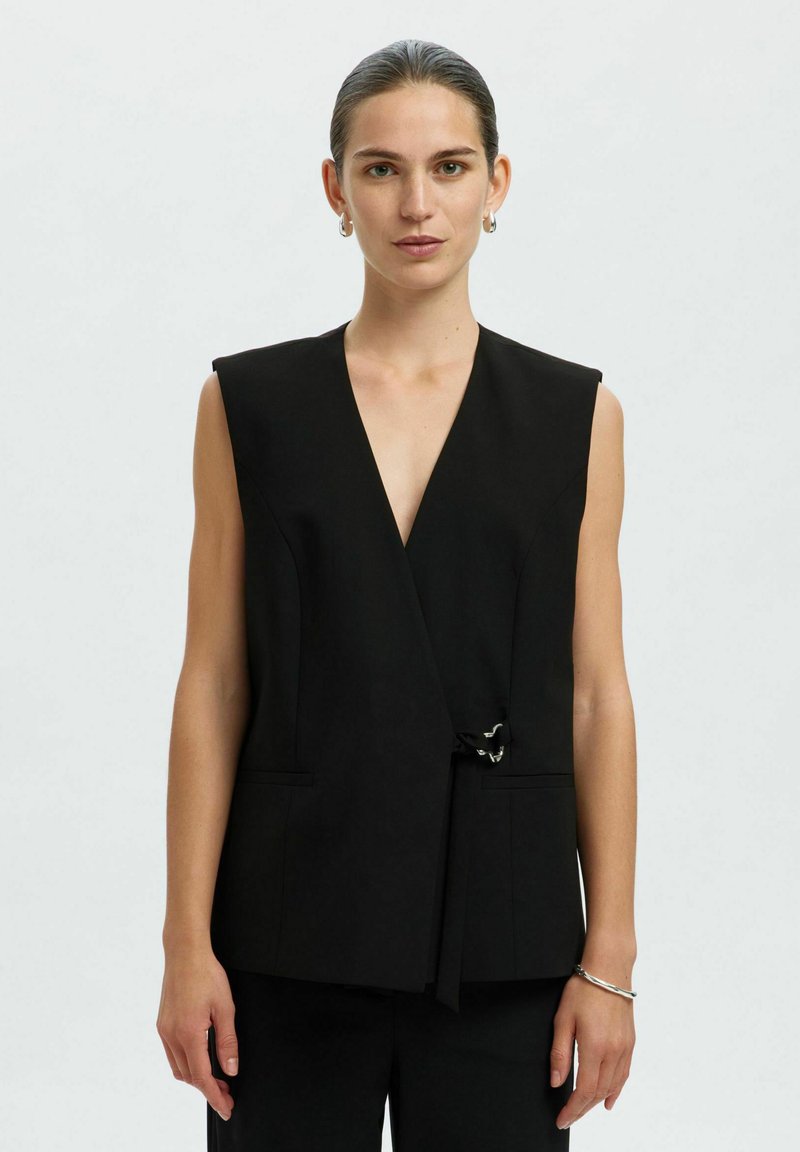 Schwarze ärmellose Wickelweste mit tiefem V-Ausschnitt, vorderem Bindedetail, zwei Taschen an den Seiten, glattem Stoff und minimalistischen Design.