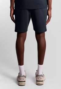 Marineblauwe shorts van zacht materiaal, met een klassieke pasvorm. Het model draagt lichtgrijze sneakers met witte sokken.
