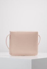 Borsa a tracolla rosa chiaro con un design minimalista, esposta su un piedistallo bianco su uno sfondo neutro.