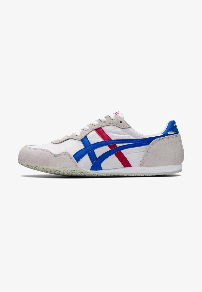Valkoiset sneakersit, joissa on harmaat mokkasuudet, siniset ja punaiset synteettiset raidat, litteät nauhat ja teksturoitu kumipohja. Klassinen muotoilu urheilullisilla elementeillä.