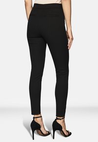 Svarta tajta byxor med en slät yta, utrustade med bakfickor och hög midja, tillsammans med svarta högklackade sandaler.