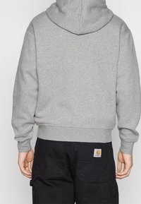 Sudadera con capucha gris de textura suave y puños acanalados, combinada con pantalones cargo negros que tienen un bolsillo de parche.