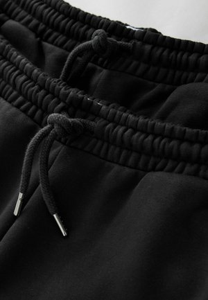 Fekete melegítőnadrág elasztikus derékpánttal, állítható húzózsinórral, sima textúrával és fémes végződésekkel a húzózsinóron.