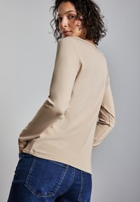 Haut beige à manches longues avec un col rond, une texture douce et une fente latérale, associé à un jean en denim bleu avec des poches arrière.