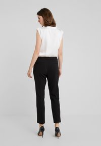 Haut sans manches blanc et pantalon noir ajusté avec poches arrière, associés à des chaussures à talons noirs. Tissu lisse, design ajusté.