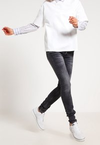 Bílý krátký rukáv top přes modré a bílé pruhované tričko, spárován se slim černými džíny a bílými teniskami. Top má hladký povrch.