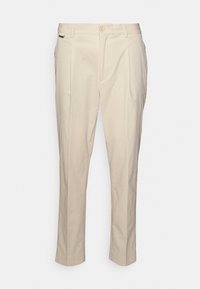 Pantaloni beige con un tessuto texturizzato, frontale plissettato e fondo con risvolto. Presentano una chiusura con bottone e tasche laterali. Design a gamba dritta.