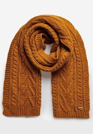 Écharpe épaisse en laine jaune moutarde tricotée avec des motifs torsadés et texturés, pliée en boucle sur un fond blanc.
