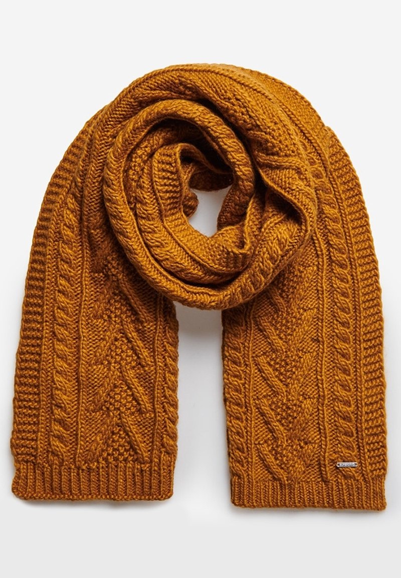 Écharpe épaisse en laine jaune moutarde tricotée avec des motifs torsadés et texturés, pliée en boucle sur un fond blanc.
