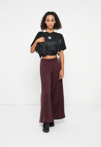 Juodas tinklinis trumpas topas su baltais akcentais, bordo plačios kojų kelnės su šoninėmis juostomis, ir mažas juodas krepšys. Savybės: tekstūruota medžiaga ir raišteliai.