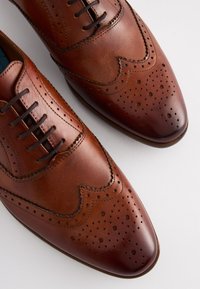 Chaussures habillées en cuir marron avec des détails brogues, bout pointu et design à lacets. Texture lisse avec perforations et coutures discrètes.