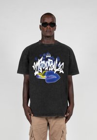 Camiseta negra de gran tamaño hecha de algodón, con un gráfico colorido en estilo graffiti de labios y un tubo, con detalles intrincados y colores vibrantes.