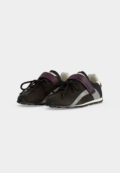 Paire de baskets noires et grises avec des bandes Velcro violettes et des lacets noirs sur fond blanc.