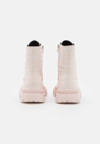 Bottes courtes couleur crème avec une texture crocodile, dotées d'une fermeture éclair latérale, d'une semelle épaisse rose et d'une finition lisse.