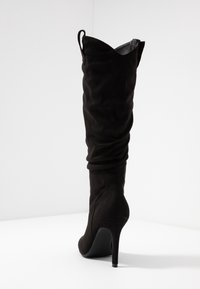 Botas de ante negro hasta la rodilla con diseño arrugado, punta afilada y tacón de aguja alto. Cuentan con una cremallera y un suave forro interior.