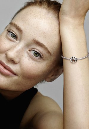 Bracciale in argento con una perla rotonda che presenta un design di impronta di zampa. Texture metallica liscia, indossato su un braccio con una tonalità di pelle chiara.