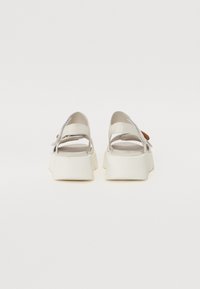 White platform sandals with an open back and adjustable ankle strap, featuring a smooth texture and rounded toe design.