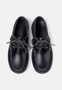 Dunkelblaue lederschuhe mit Schnürsenkeln, die kontrastierende weiße Nähte und perforierte Einlagen aufweisen, aus der Vogelperspektive vor einem hellen Hintergrund präsentiert.
