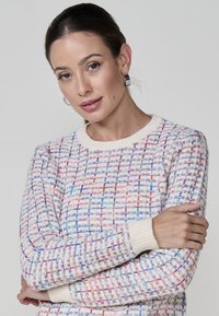 Pull en maille avec un motif tissé en crème, présentant des accents colorés en rose, violet et bleu. Encolure ronde et poignets côtelés.