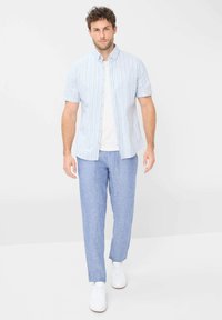 Korte mouwen overhemd met blauw en witte verticale strepen, gecombineerd met lichtblauwe broek en witte sneakers. Eenvoudig, casual ontwerp.