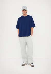 Námornícka oversized tričko s logom, šedé teplákové nohavice a šedá čiapka. Tenisky sú v kombinácii farieb a textúr. Jednoduchý, ležérny outfit.