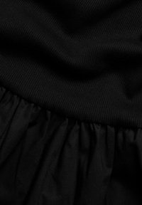 Sort kjole med et ribbet bodice og en svævende, flæset nederdel. Stoffet fremstår glat med en let tekstur, helt i dyb sort.
