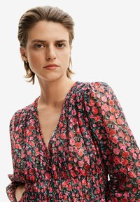 Abito floreale caratterizzato da un tessuto trasparente e leggero con uno sfondo nero e fiori vivaci rossi e rosa. Scollo a V e vita elasticizzata.