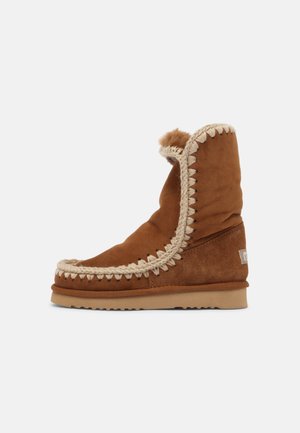 Braune Wildleder-Stiefeletten mit dekorativer beiger Naht entlang der Kanten, flauschigem Innenfutter und einer flachen Gummisohle.