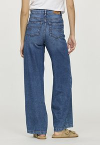 Jeans en denim bleu à jambes larges et taille haute, avec des poches arrière, une étiquette en cuir à la taille et une finition texturée classique.