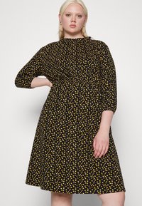 Vestido preto com bolinhas amarelas, mangas curtas, cintura ajustada e saia rodada. Tecido suave com um brilho subtil.