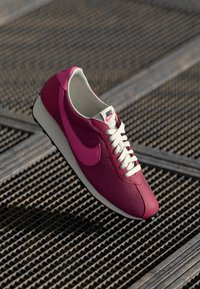Nike Sneaker mit einem oberen Teil aus pinkem Mesh, kontrastierenden pinken Akzenten, weißen Schnürsenkeln und einer strukturierten Sohle. Leichtes Design für Komfort und Stil.