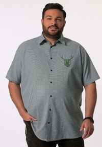 Camisa de manga corta con botones en un patrón de cuadros verde y negro, que presenta un logo de ciervo verde en el lado izquierdo del pecho. Hecha de una tela liviana.