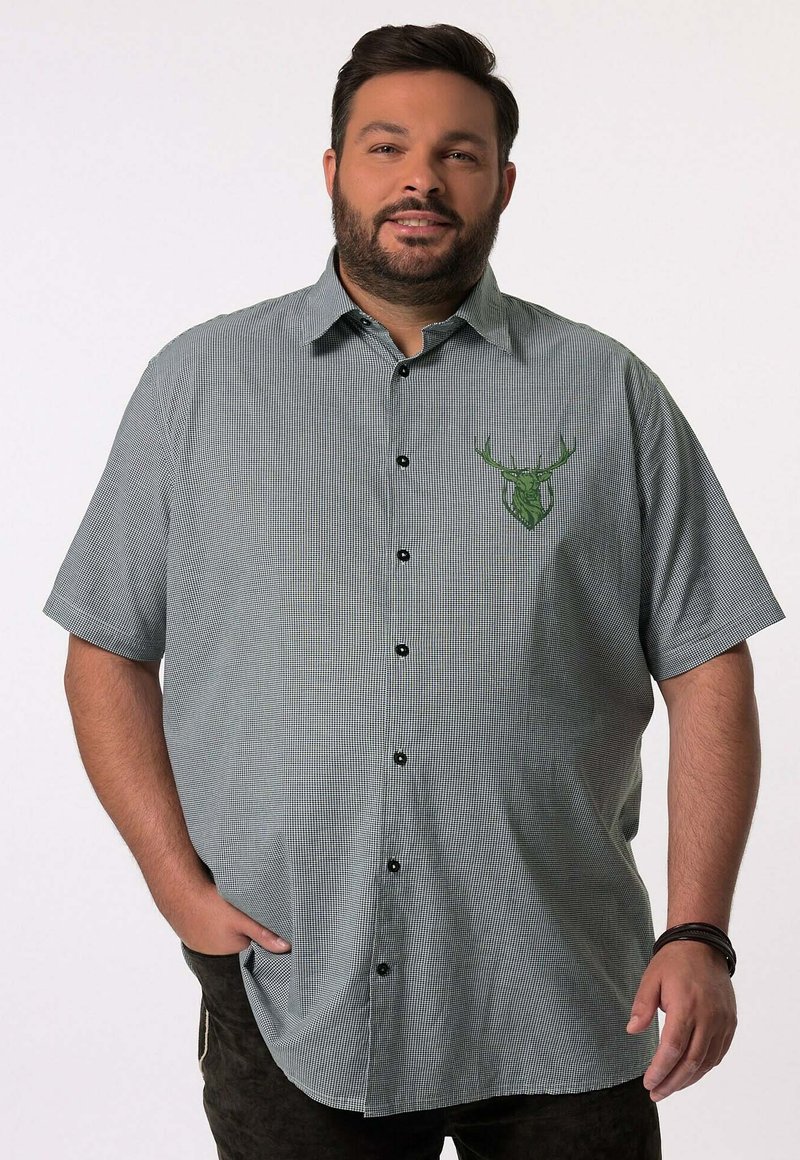 Camisa de manga corta con botones en un patrón de cuadros verde y negro, que presenta un logo de ciervo verde en el lado izquierdo del pecho. Hecha de una tela liviana.