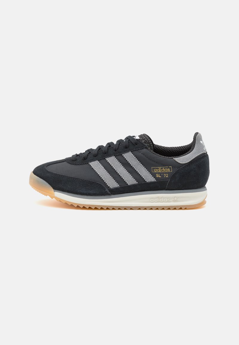 Sapatilha em camurça preta e malha com três riscas cinzas, sola de borracha cinza e branding dourado na lateral. Design retro clássico.