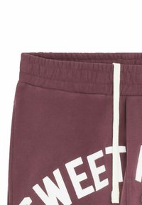 Pantalons de survêtement bordeaux avec cordon blanc, présentant le texte "SWEET" en gras sur la jambe gauche. Matériau en coton doux avec une taille élastique.
