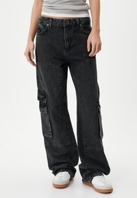 Zwarte denim cargobroek met een losse pasvorm, voorzien van meerdere zakken, contrasterende stiksels en een vervaagde afwerking. Gesterkt met witte sneakers.