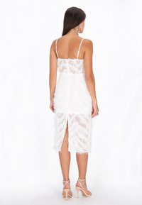 Rochie midi albă din pene, cu bretele subțiri, material transparent, straturi texturate și slit la spate. Asortată cu sandale cu toc nude.