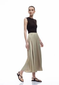 Brun ærmeløs top, beige plissee maxi nederdel med elastisk talje og sorte flade sandaler. Glat stof og flydende design.
