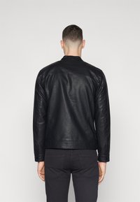 Chaqueta de cuero negra con una textura suave, diseño ajustado y un pequeño collar. Presenta costuras en la parte trasera y en las mangas.