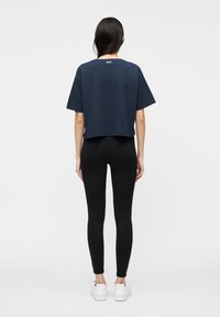 T-shirt azul-marinho cropped feita de algodão, com mangas curtas e decote redondo. Combinada com leggings pretas e sapatilhas brancas.