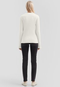 Biały prążkowany sweter z długimi rękawami, zestawiony z czarnymi jeansami o dopasowanym kroju i jasnymi butami wsuwanymi, widok od tyłu.