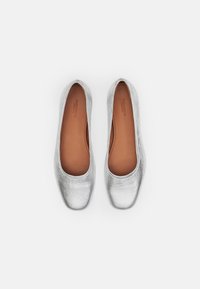 Silver balletfötter med en slät metallisk yta och rund tå. Insidan har en tan-färgad sula. Ingen synlig hårdvara eller dekorationer.