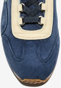 Sneaker in camoscio navy con un accento in pelle crema, caratterizzato da lacci scuri e occhielli metallici. Dettaglio di cucitura notevole e suola testurizzata.