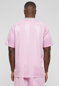 Pink sports jersey with subtle vertical stripes, short sleeves, and a white collar. Smooth texture with a relaxed fit.