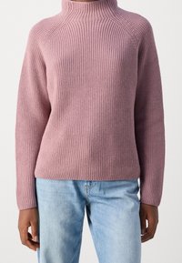 Knitted pullover sweater in mauve with a high neckline, ribbed texture, and long sleeves, paired with light blue jeans.