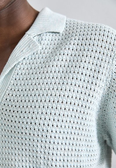Suéter de polo de manga corta de color azul claro, tejido con un diseño de trama texturada y un cuello acanalado.