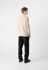 Beige bordázott pulóver kerek nyakkivágással, fekete laza nadrággal és fekete csizmával viselve. Az anyag textúrája érződik, melegnek tűnik.