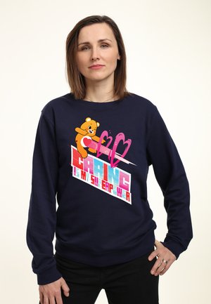 Námořnický modrý svetr vyrobený z bavlněné směsi s grafickým designem zobrazujícím medvěda, srdce a barevný text. Dlouhé rukávy a uvolněný střih.