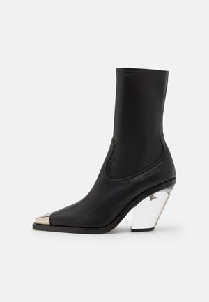 Czarne skórzane botki za kostkę z ostrym noskiem, metalicznie złotą czapeczką i przezroczystym geometrycznym obcasem. Gładka tekstura, elegancki design.